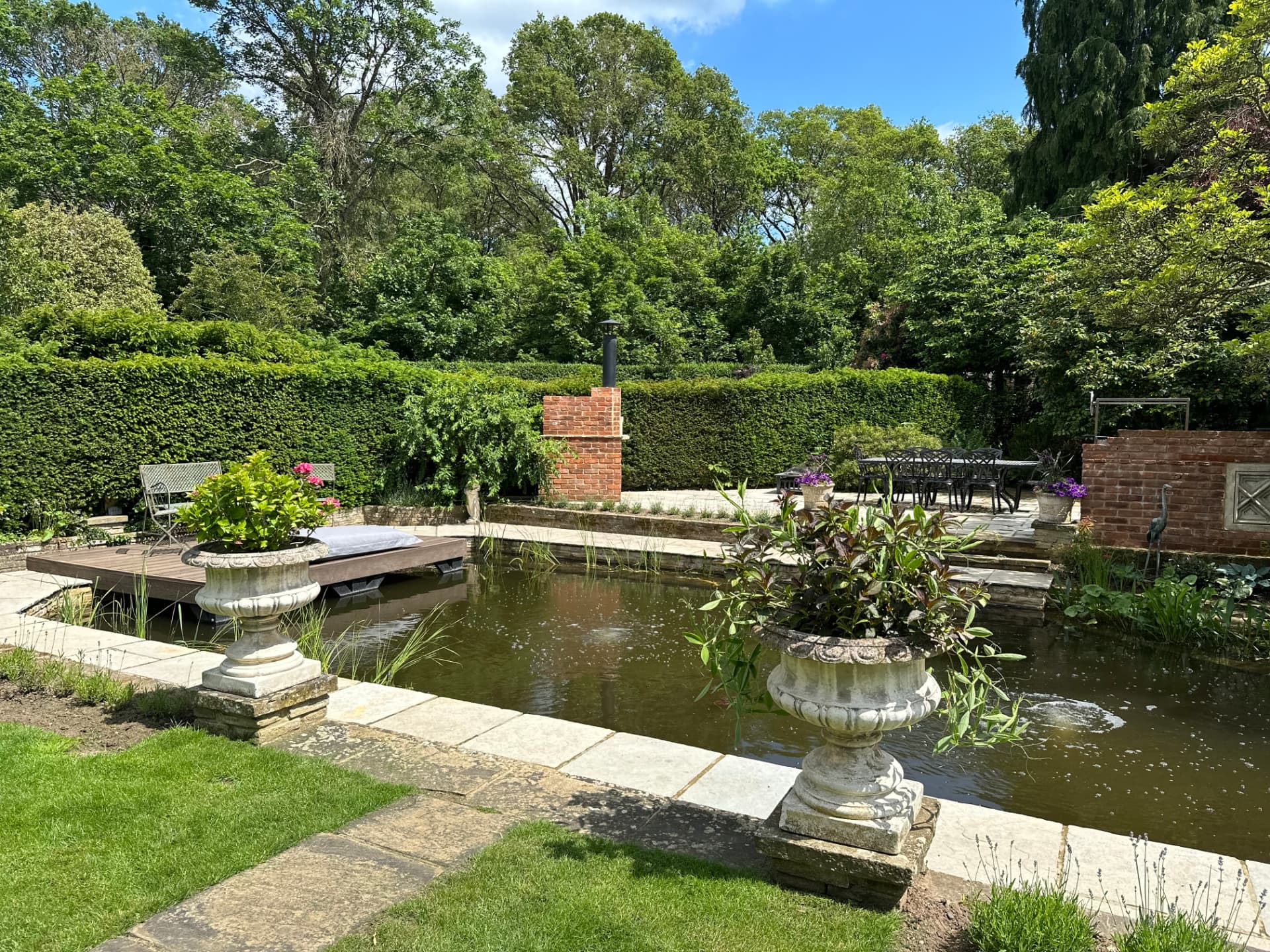 A formal garden pond edged with stone paving, urns and a brick feature wall