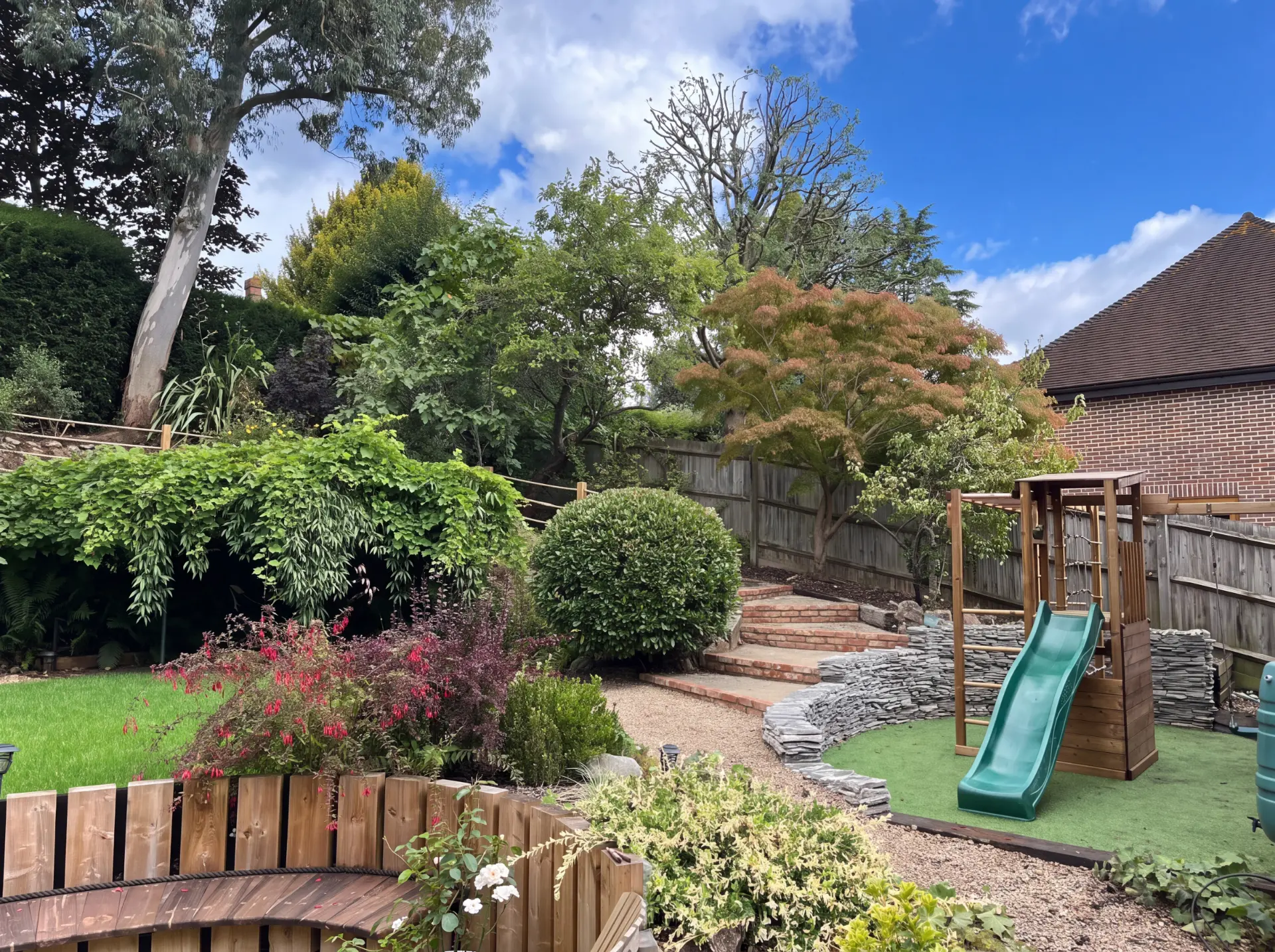 A family garden with brick steps, dry stone retaining walls and a play area