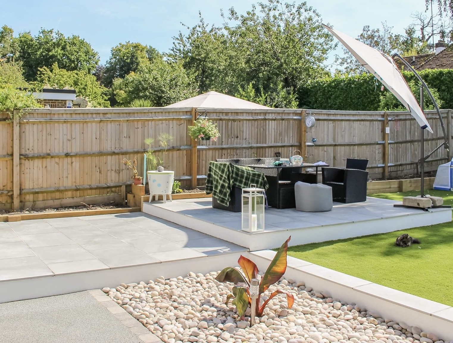 A raised porcelain patio with a dining area, pebble bed and lawn
